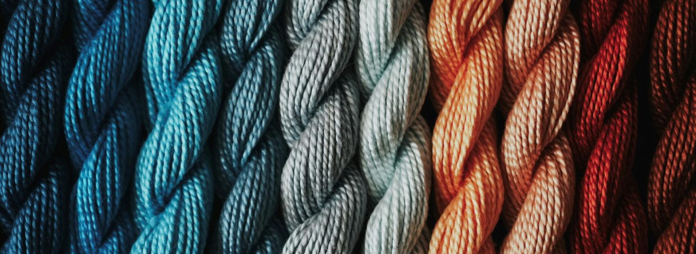 Wool skeins displayed beside each other to make a beautiful gradient of red, peach, light blue, bright blue, and dark blue